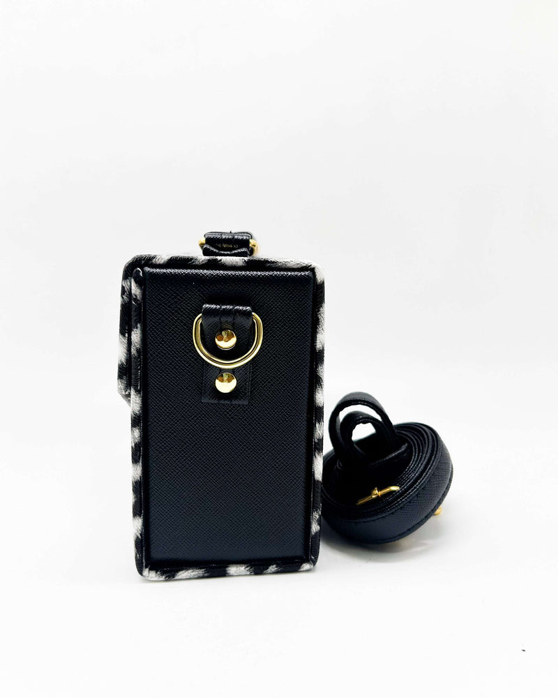 Side view, black and white animal print vegan leather handbag with a gold buckle clasp and adjustable strap.