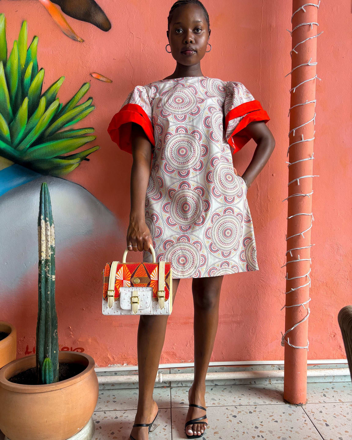 African woman wearing a Sam Dress in off white and red, with a Dr Pachanga handbag and black high heels.