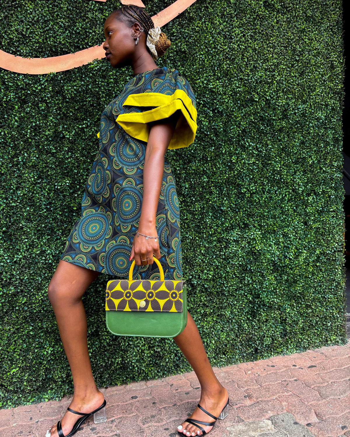 African woman wearing a Sam Dress in green, with a Dr Pachanga handbag and black high heels.