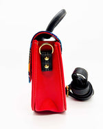 Side view, red vegan leather handbag with blue and yellow African Gold Wax fabric inlay, gold magnetic clasp and adjustable strap.