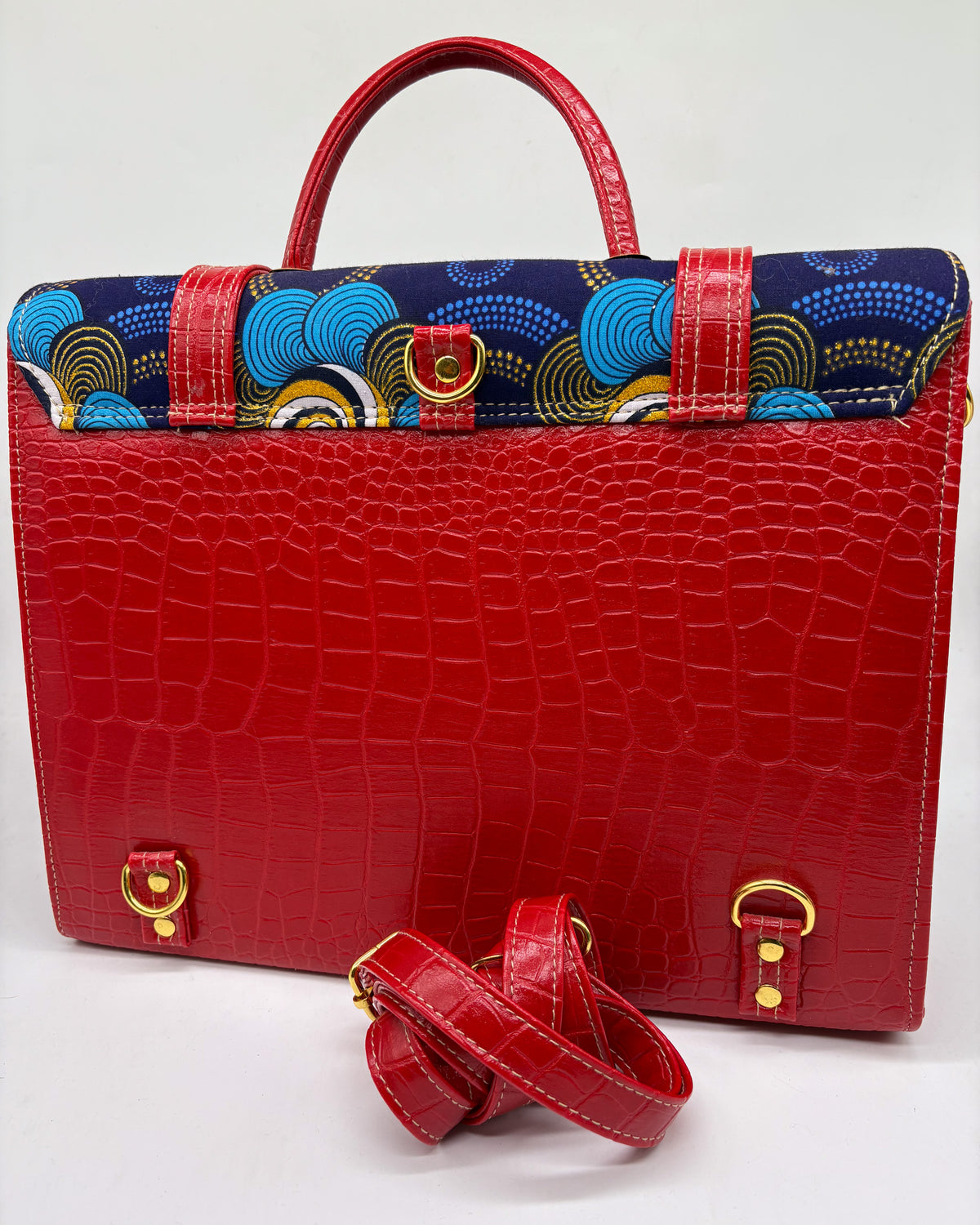 Back angle, red vegan leather handbag or backpack with gold and blue African wax fabric inlay, two gold buckled clasps and gold twist-lock.