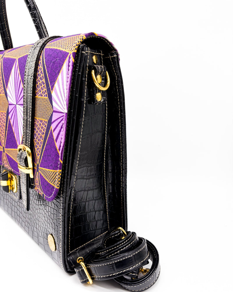 Side angle, black vegan leather handbag or backpack with purple and yellow African wax fabric inlay, two gold buckled clasps and a gold twist-lock.