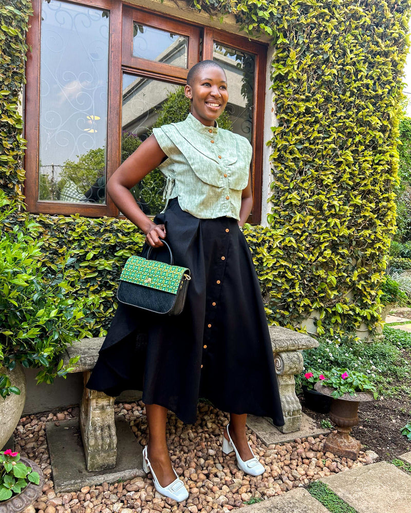 Smiling African woman wearing a Zandi Skirt in black with a Dr Pachanga handbag, and white heeled shoes.
