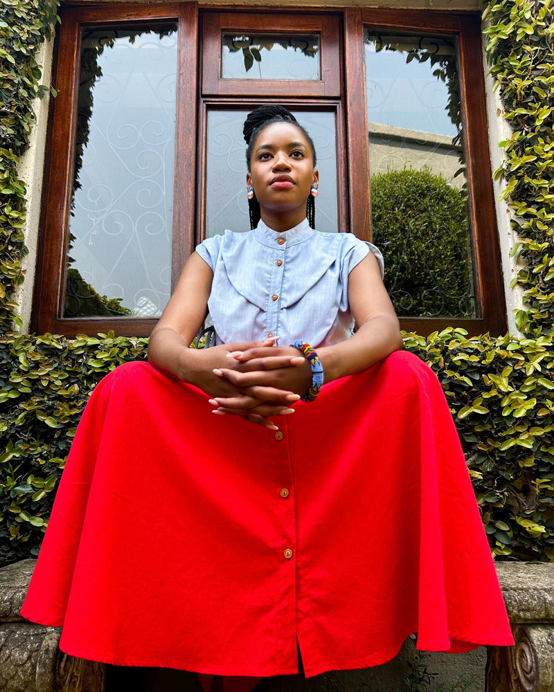African woman sitting, wearing a Zandi Skirt in blood orange.