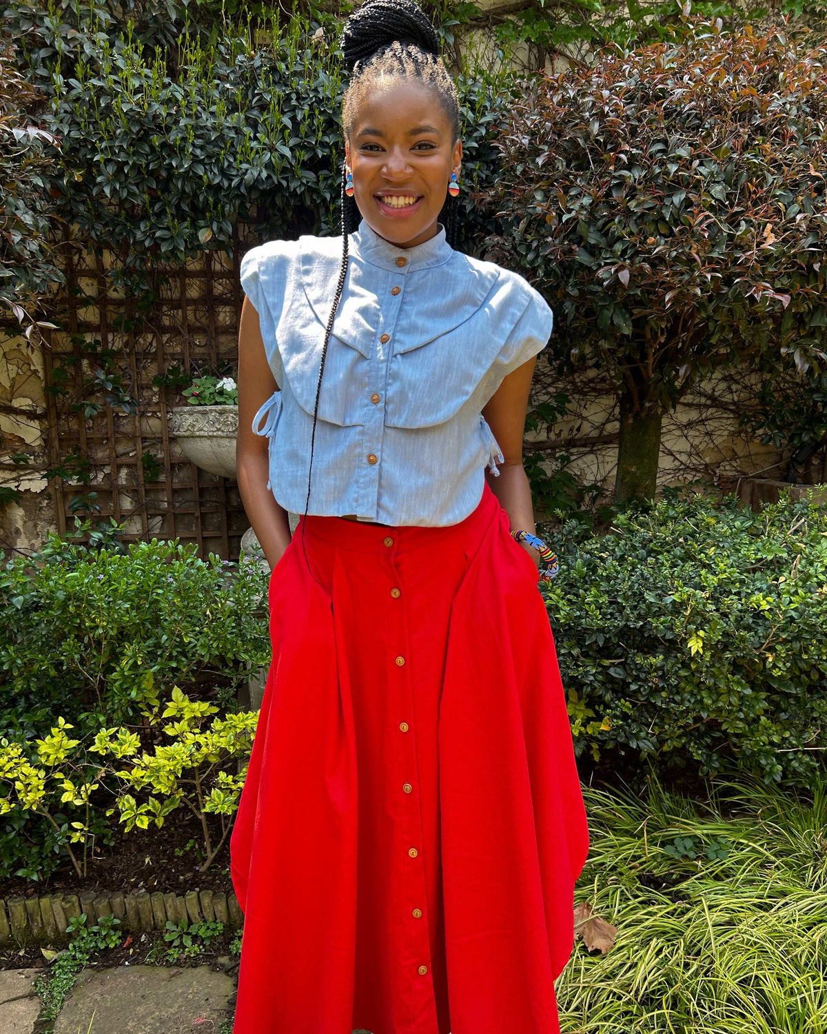 Smiling African woman wearing a Zandi Skirt in blood orange, with hands in her pockets.
