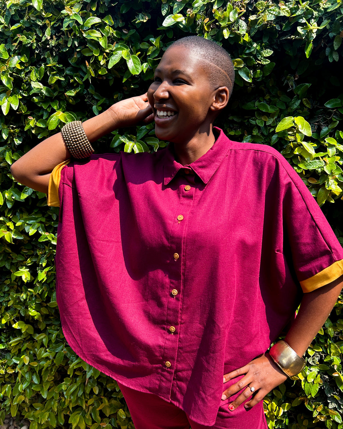 Close-up, smiling African woman wearing a maroon and mustard Marcelle Top.