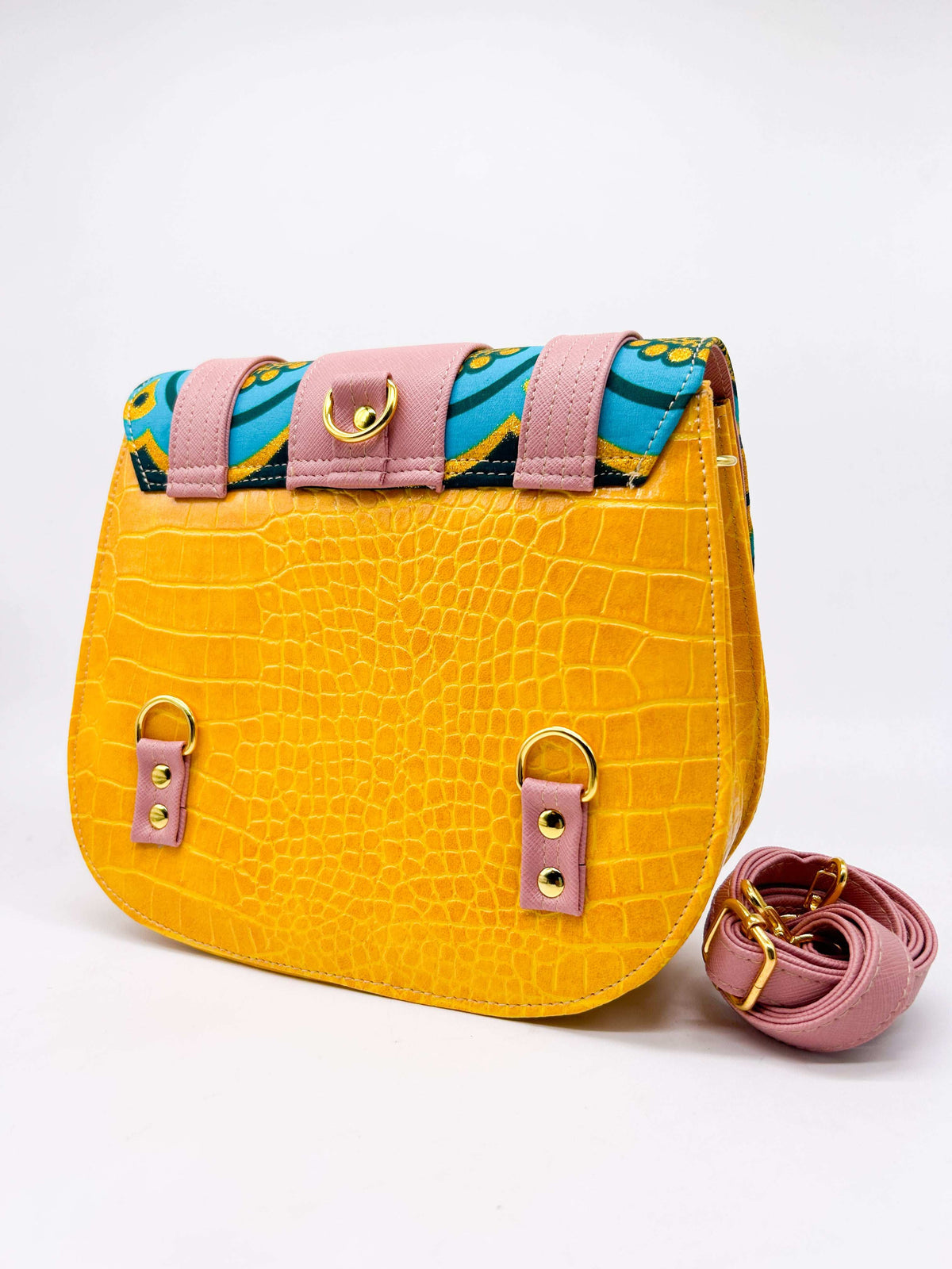Back view, orange textured vegan leather handbag with pink accents and blue and yellow African Gold Wax fabric inlay, a magnetic clasp and adjustable strap.