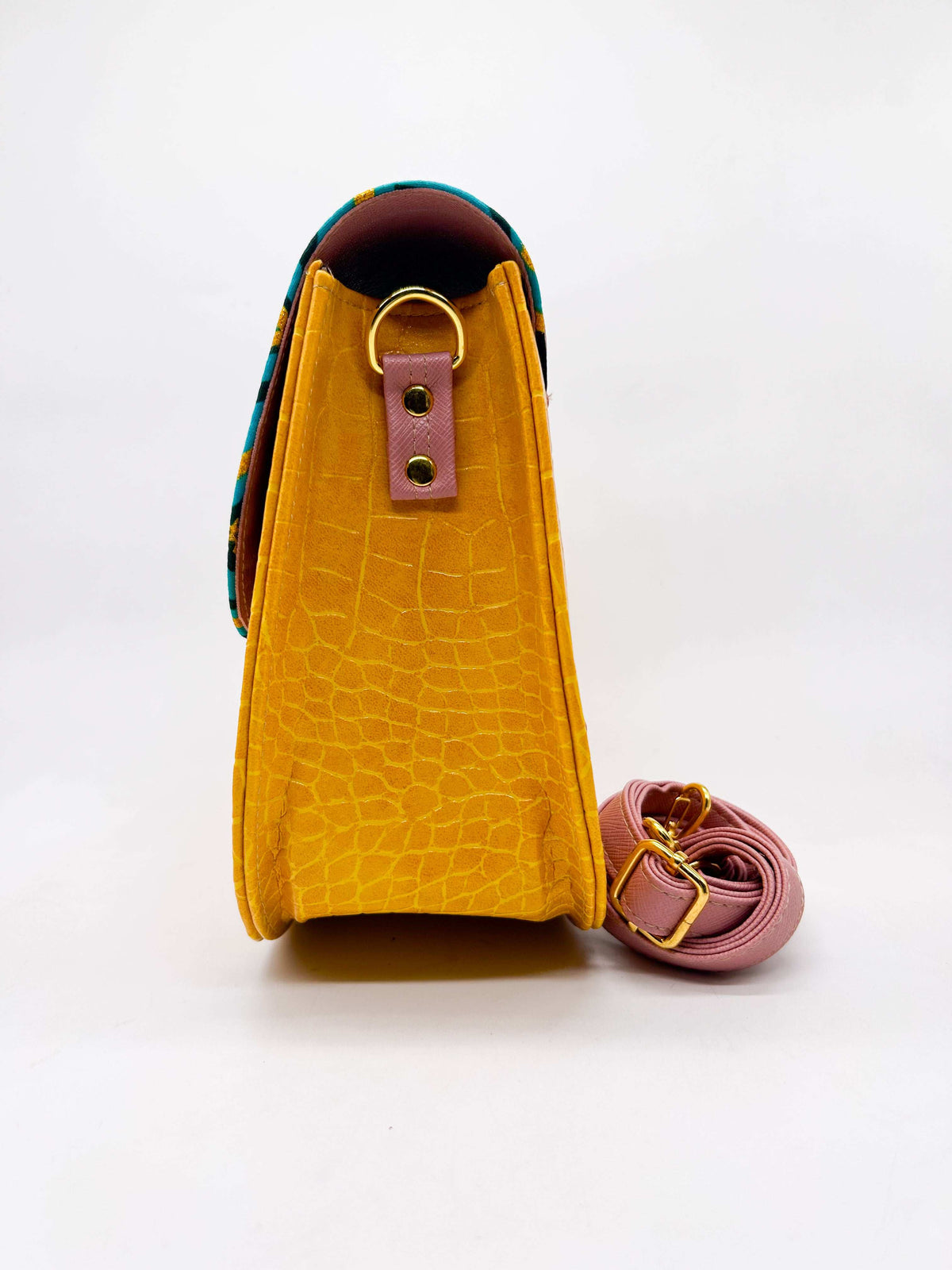 Side view, orange textured vegan leather handbag with pink accents and blue and yellow African Gold Wax fabric inlay, a magnetic clasp and adjustable strap.