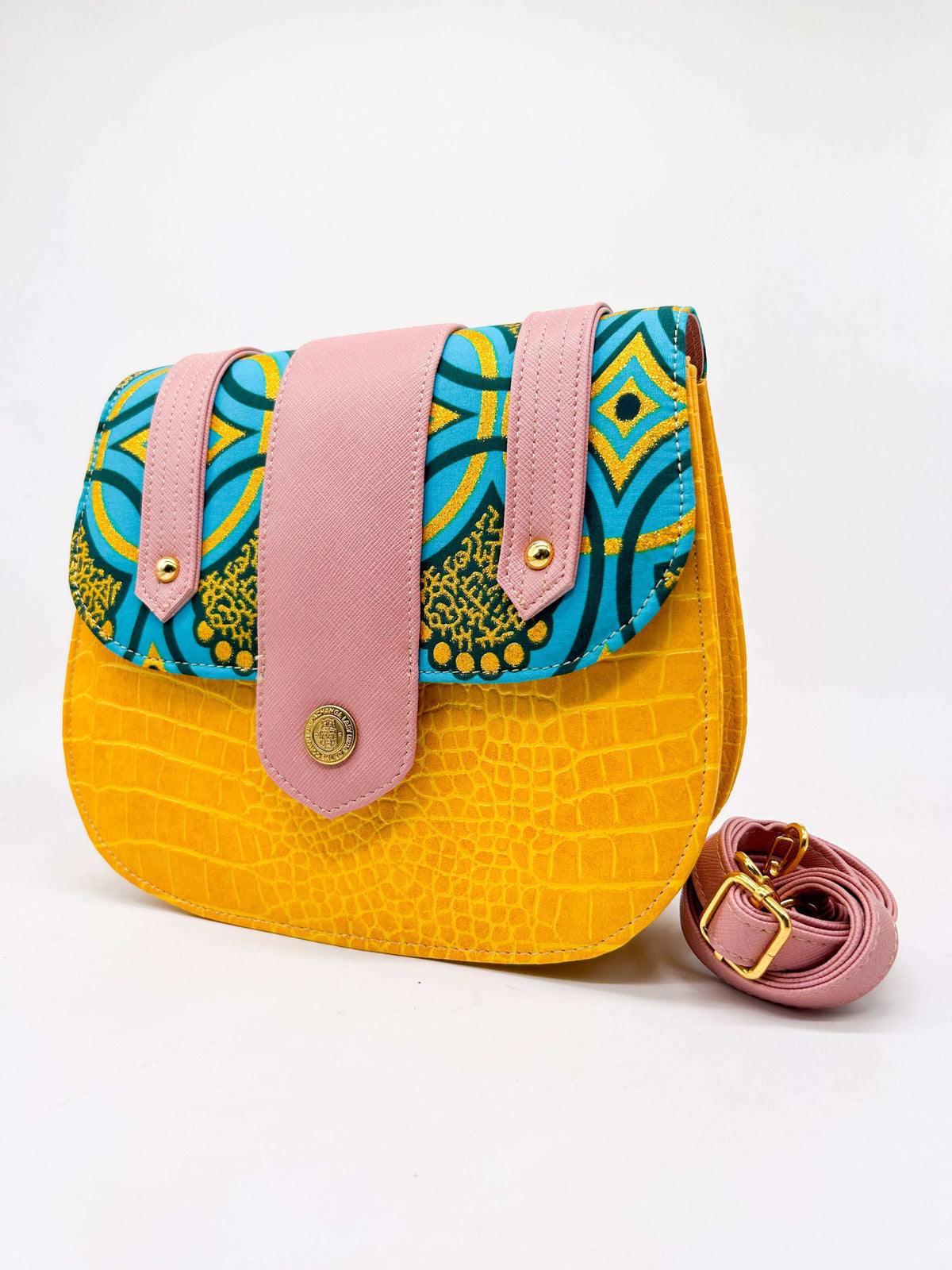 Orange textured vegan leather handbag with pink accents and blue and yellow African Gold Wax fabric inlay, a magnetic clasp and adjustable strap.