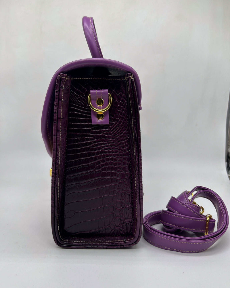 Side view, purple vegan leather handbag with yellow and brown African Wax fabric inlay, a buckled strap, gold magnetic clasp and adjustable strap. 