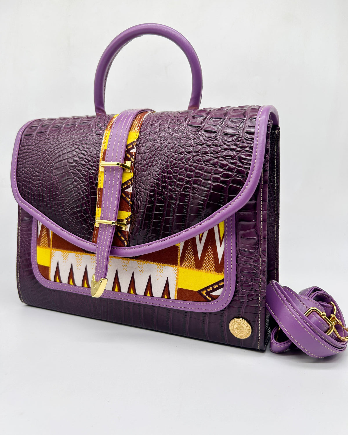 Purple vegan leather handbag with yellow and brown African Wax fabric inlay, a buckled strap, gold magnetic clasp and adjustable strap. 