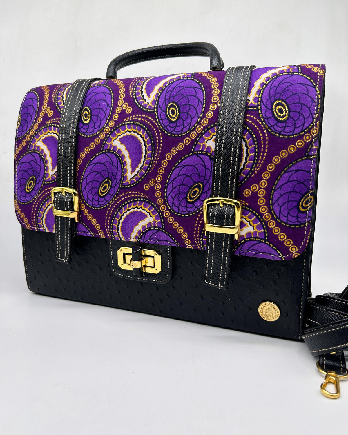 Black vegan leather handbag or backpack with gold and purple African wax fabric inlay, two gold buckled clasps and gold twist-lock.