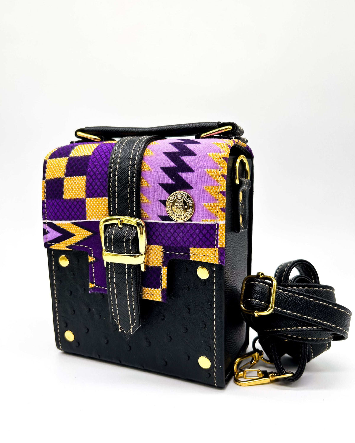 Black vegan leather handbag with yellow and purple African Gold Wax fabric inlay, a single gold buckle, magnetic clasp and adjustable strap.