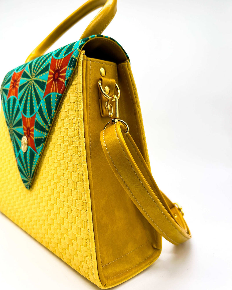 Side view, yellow textured vegan leather handbag with green and red African Gold Wax fabric inlay, a magnetic clasp and adjustable strap.