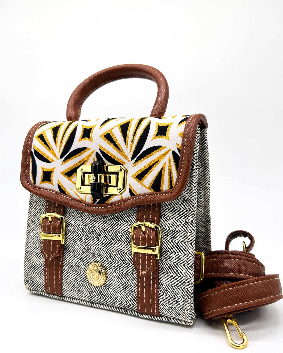 Black and white vegan leather handbag or crossbody bag with black and orange African wax fabric inlay, two gold buckled clasps and a twist-lock.