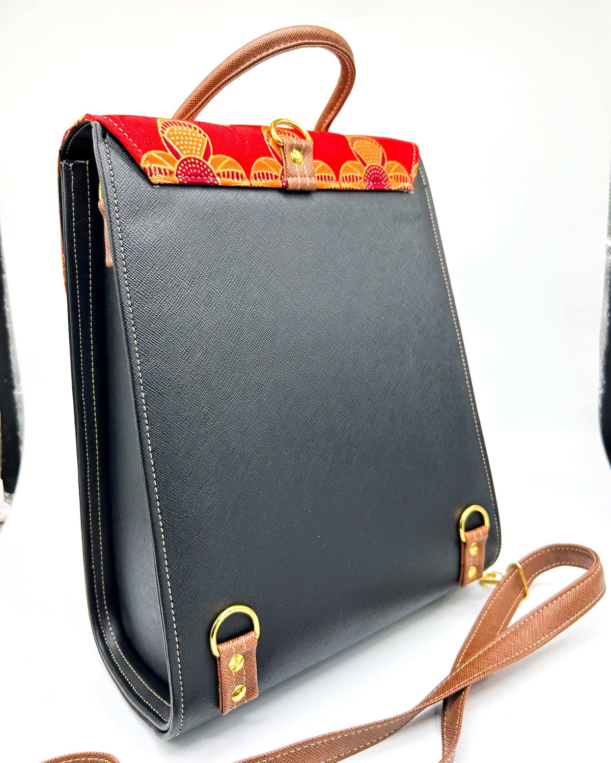 Back view, black vegan leather handbag with brown accents and yellow and red African Gold Wax fabric inlay, two gold buckles, a twist-lock clasp and adjustable strap.