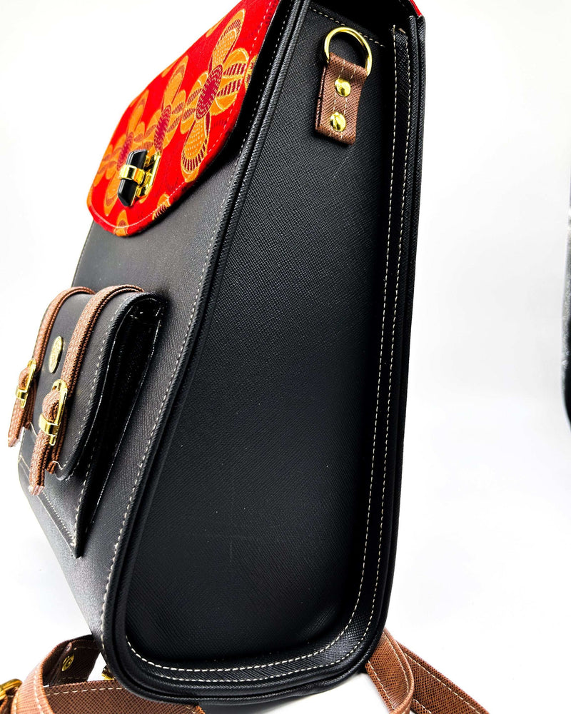 Side view, black vegan leather handbag with brown accents and yellow and red African Gold Wax fabric inlay, two gold buckles, a twist-lock clasp and adjustable strap.