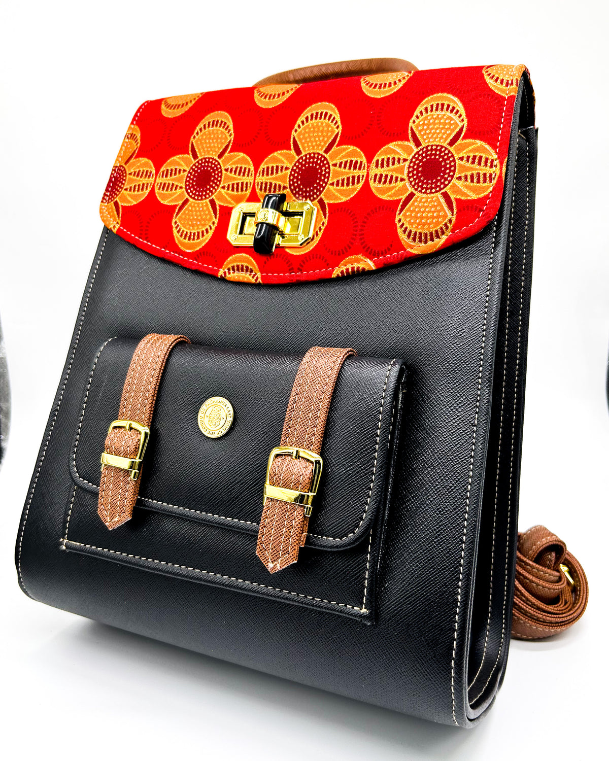 Black textured vegan leather handbag with brown accents and yellow and red African Gold Wax fabric inlay, two gold buckles, a twist-lock clasp and adjustable strap.