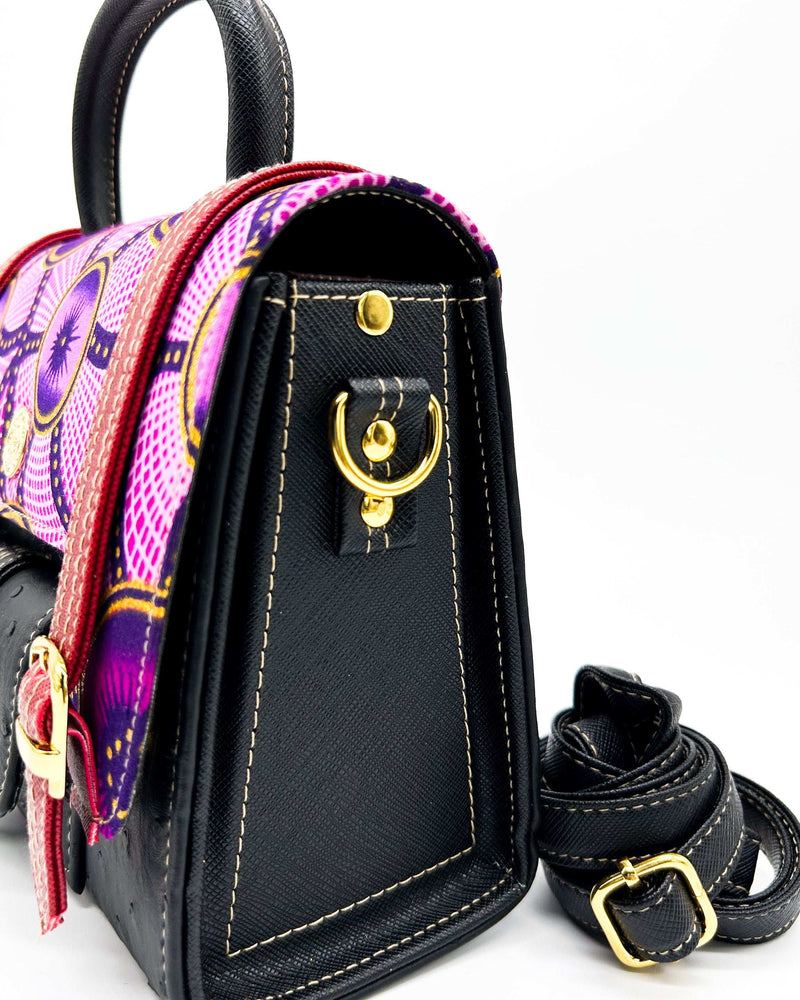 Side angle, black vegan leather handbag, backpack or crossbody bag with pink and yellow African wax fabric inlay and three gold buckled clasps.