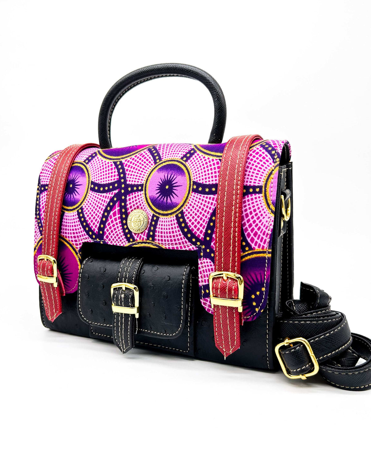 Front angle, black vegan leather handbag, backpack or crossbody bag with pink and yellow African wax fabric inlay and three gold buckled clasps.
