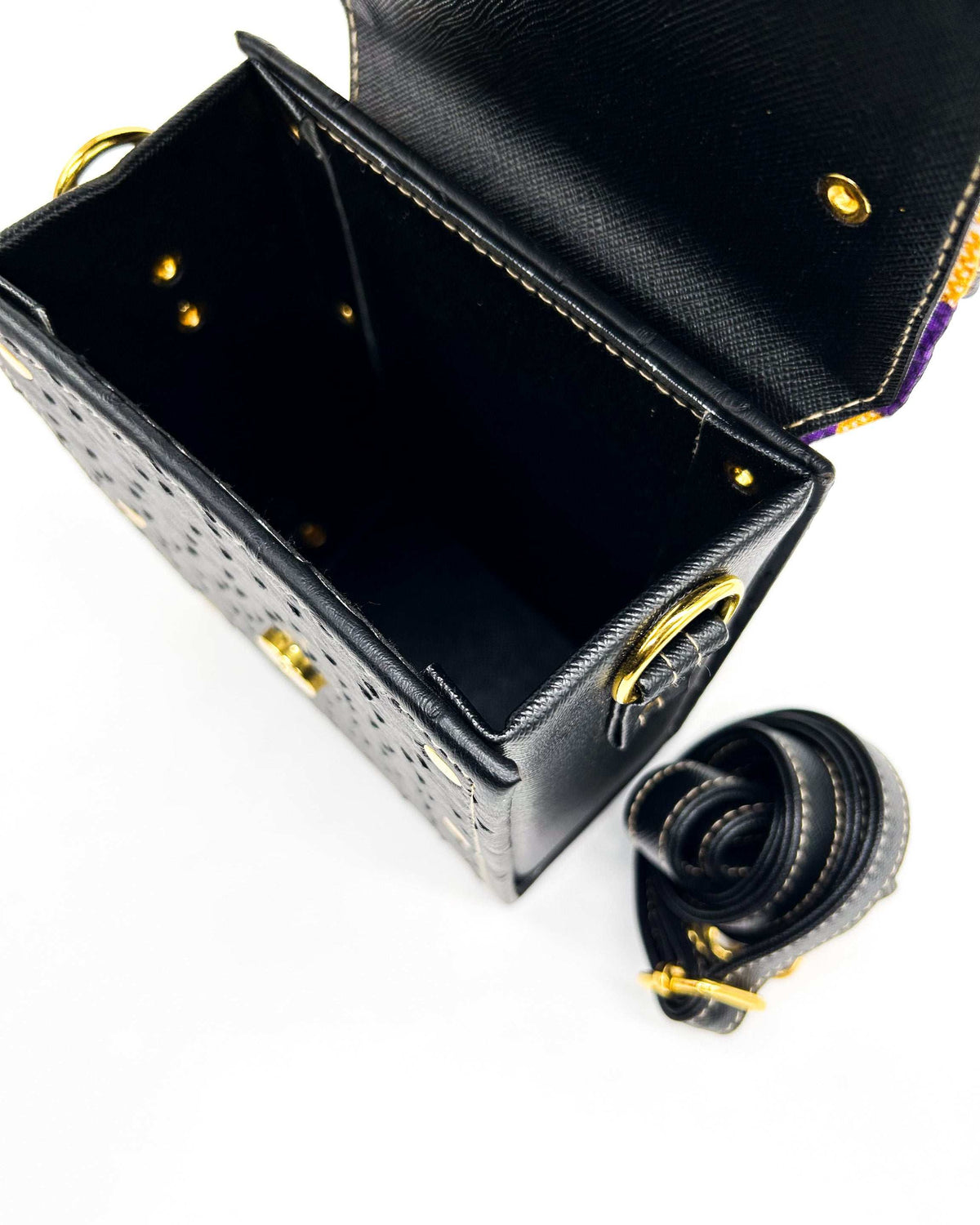 Inside view, black vegan leather handbag with yellow and purple African Gold Wax fabric inlay, a single gold buckle, magnetic clasp and adjustable strap.