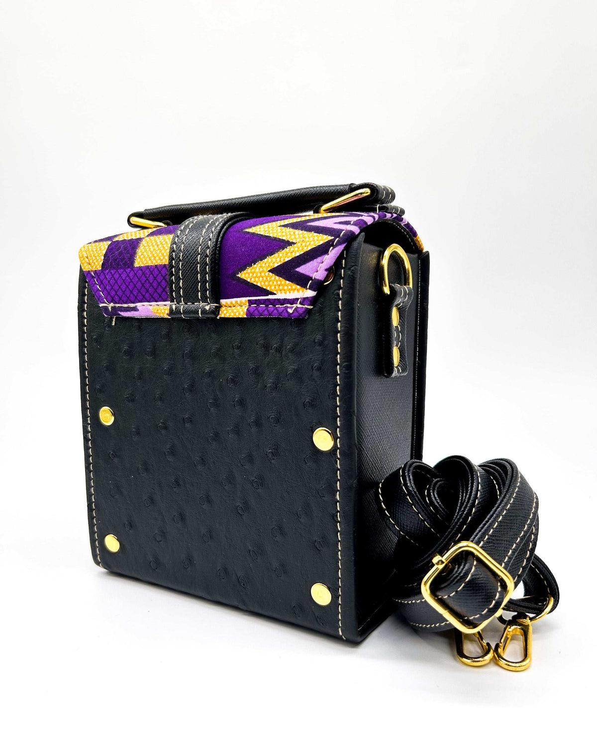 Back view, black vegan leather handbag with yellow and purple African Gold Wax fabric inlay, a single gold buckle, magnetic clasp and adjustable strap.