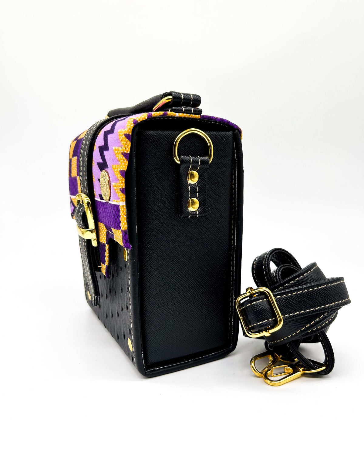 Side view, black vegan leather handbag with yellow and purple African Gold Wax fabric inlay, a single gold buckle, magnetic clasp and adjustable strap.