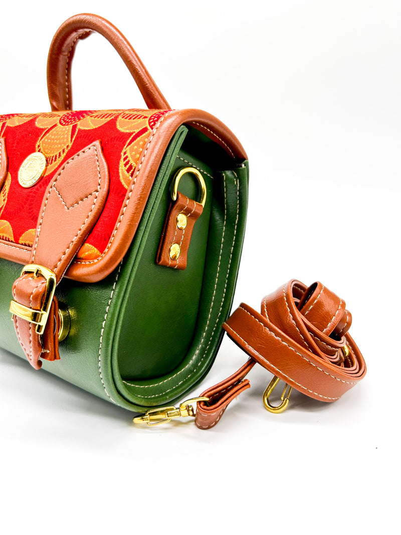 Side angle, olive green vegan leather handbag or backpack with red and orange African wax fabric inlay and two buckled clasps.