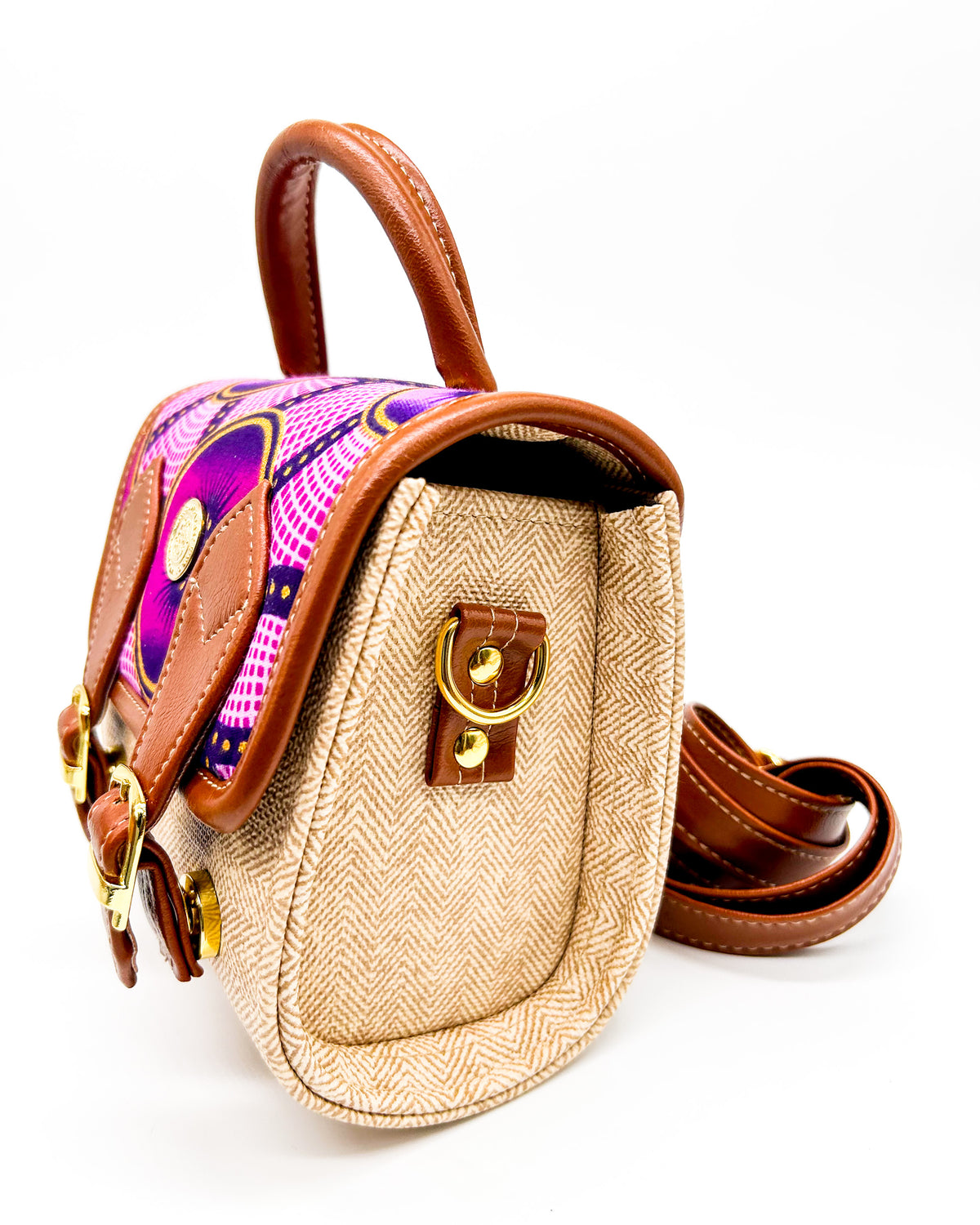 Side angle, beige vegan leather handbag or backpack with pink and yellow African wax fabric inlay and two buckled clasps.