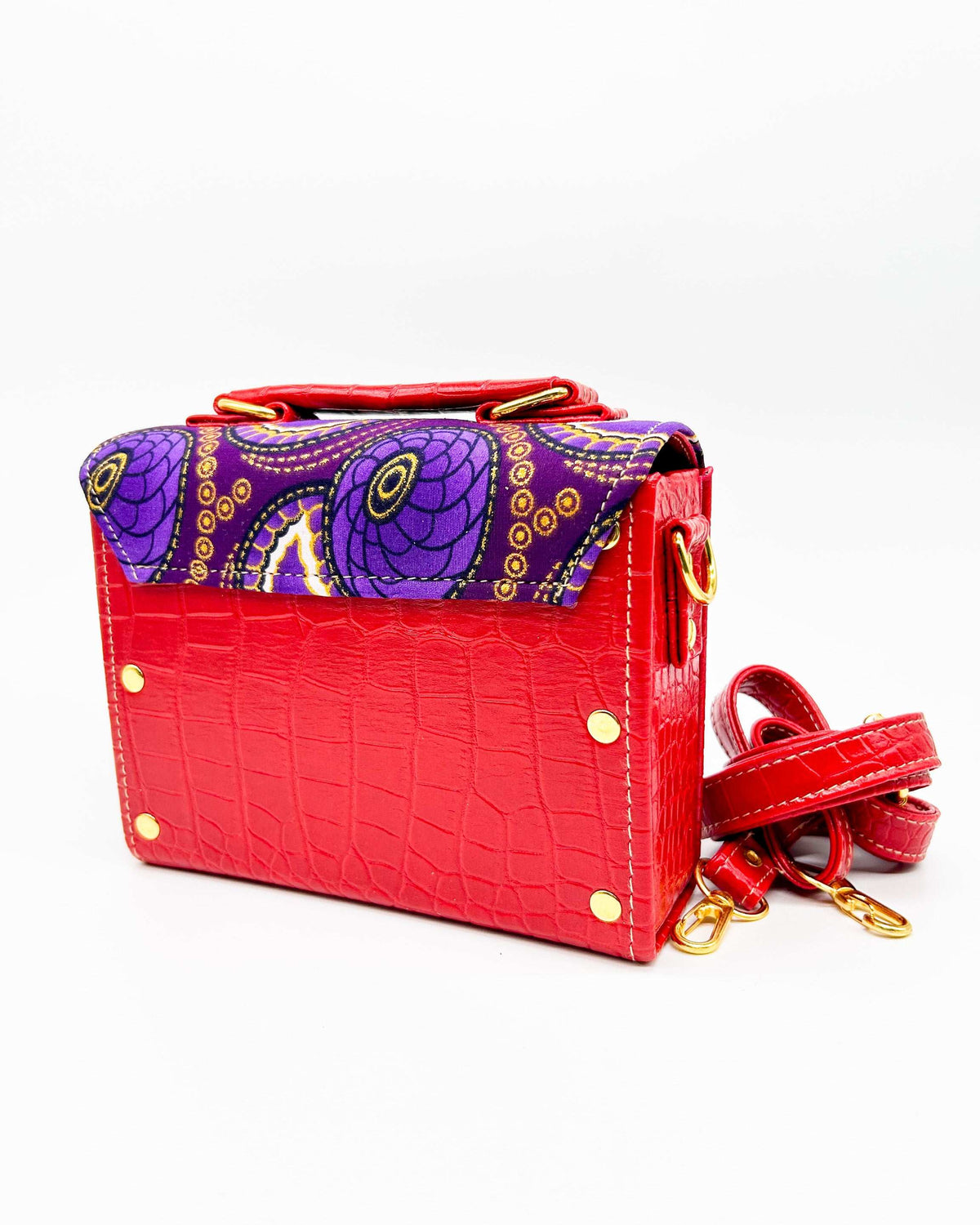 Back angle, red vegan leather handbag, backpack or crossbody bag with purple and yellow African wax fabric inlay and two gold buckled clasps.
