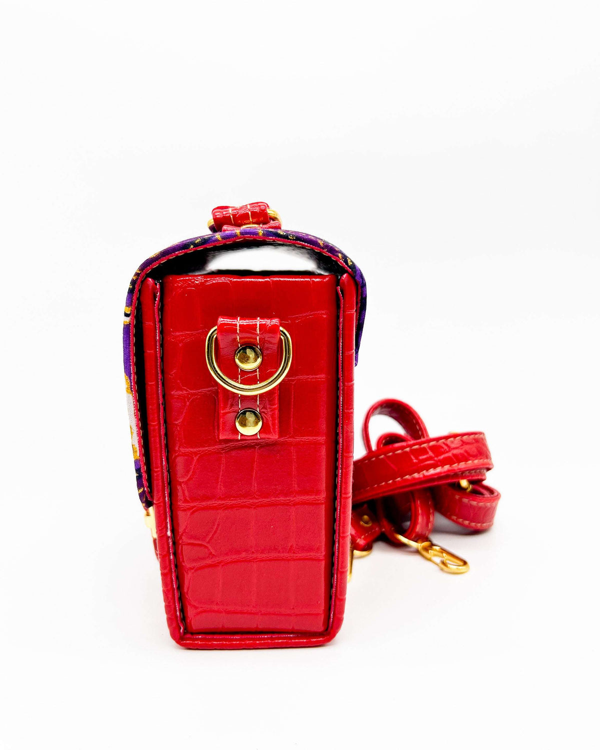Side angle, red vegan leather handbag, backpack or crossbody bag with purple and yellow African wax fabric inlay and two gold buckled clasps.