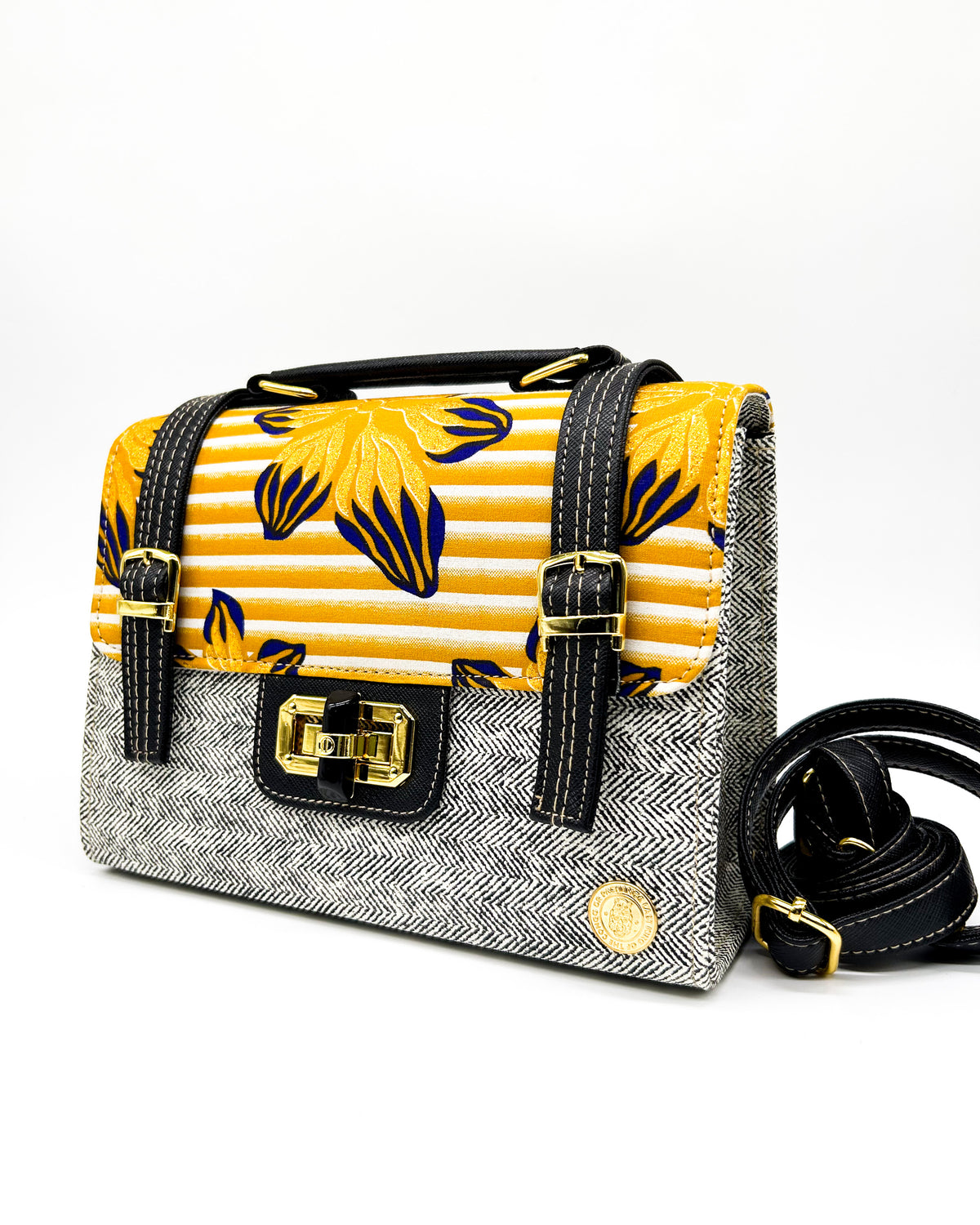 Grey vegan leather handbag with yellow and orange African Gold Wax fabric inlay, two gold buckled straps, a twist-lock clasp and adjustable strap.