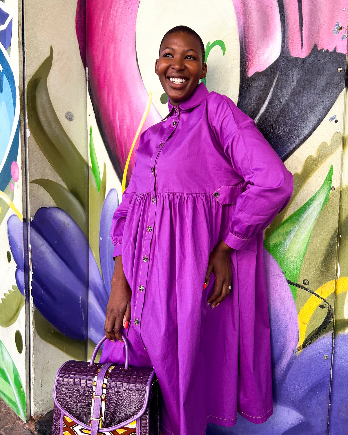 Smiling African woman wearing a Mimi Dress in purple, with a Dr Pachanga handbag.