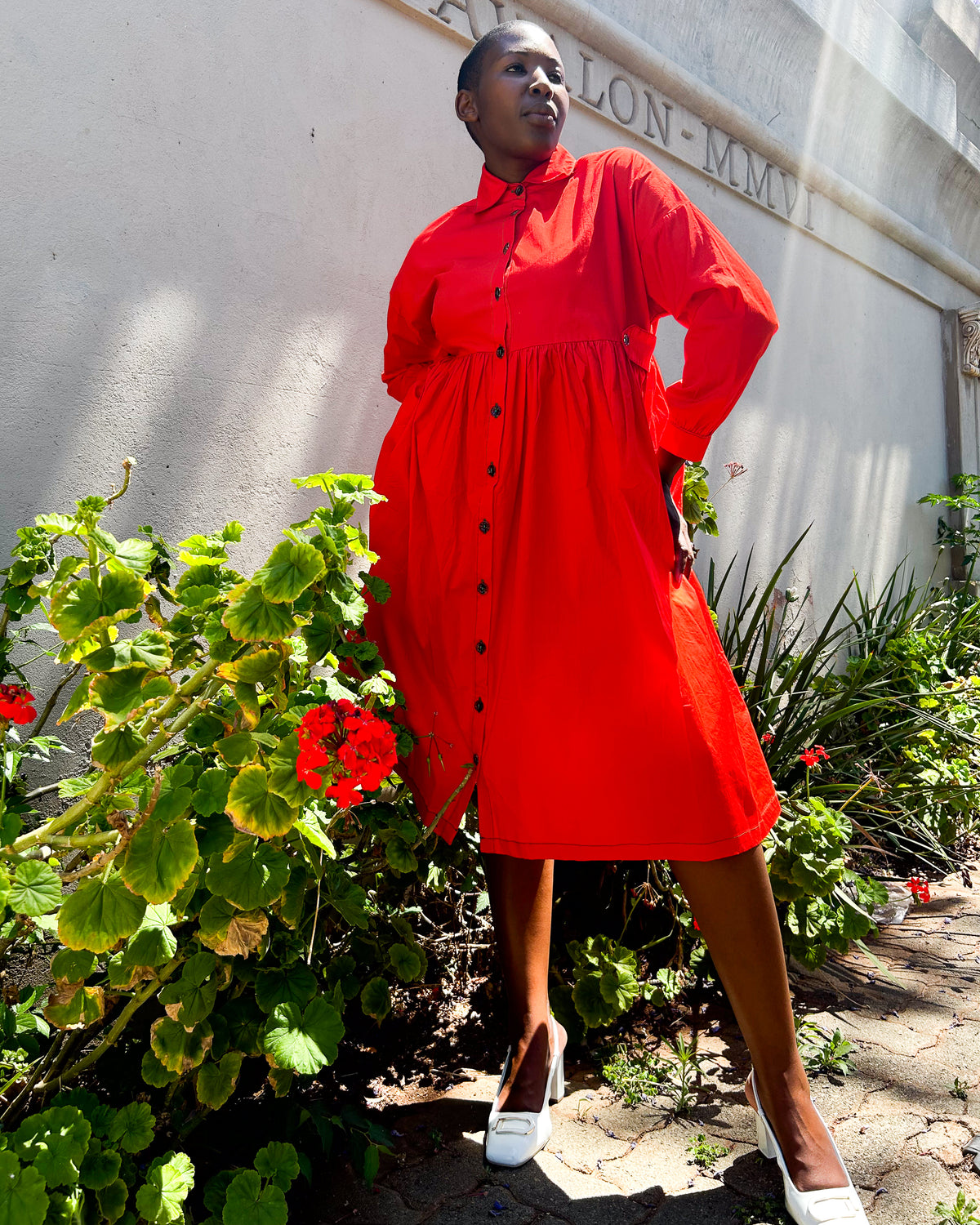 African woman wearing a Mimi Dress in orange, with white heled shoes.