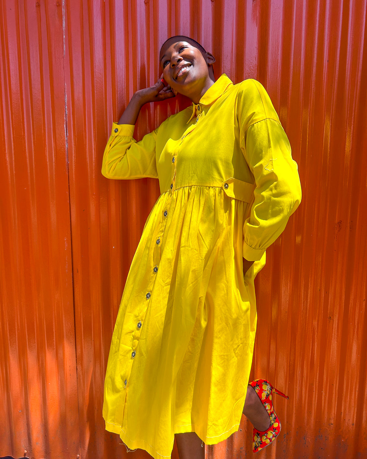 African woman wearing a Mimi Dress in yellow, with colourful high heels.