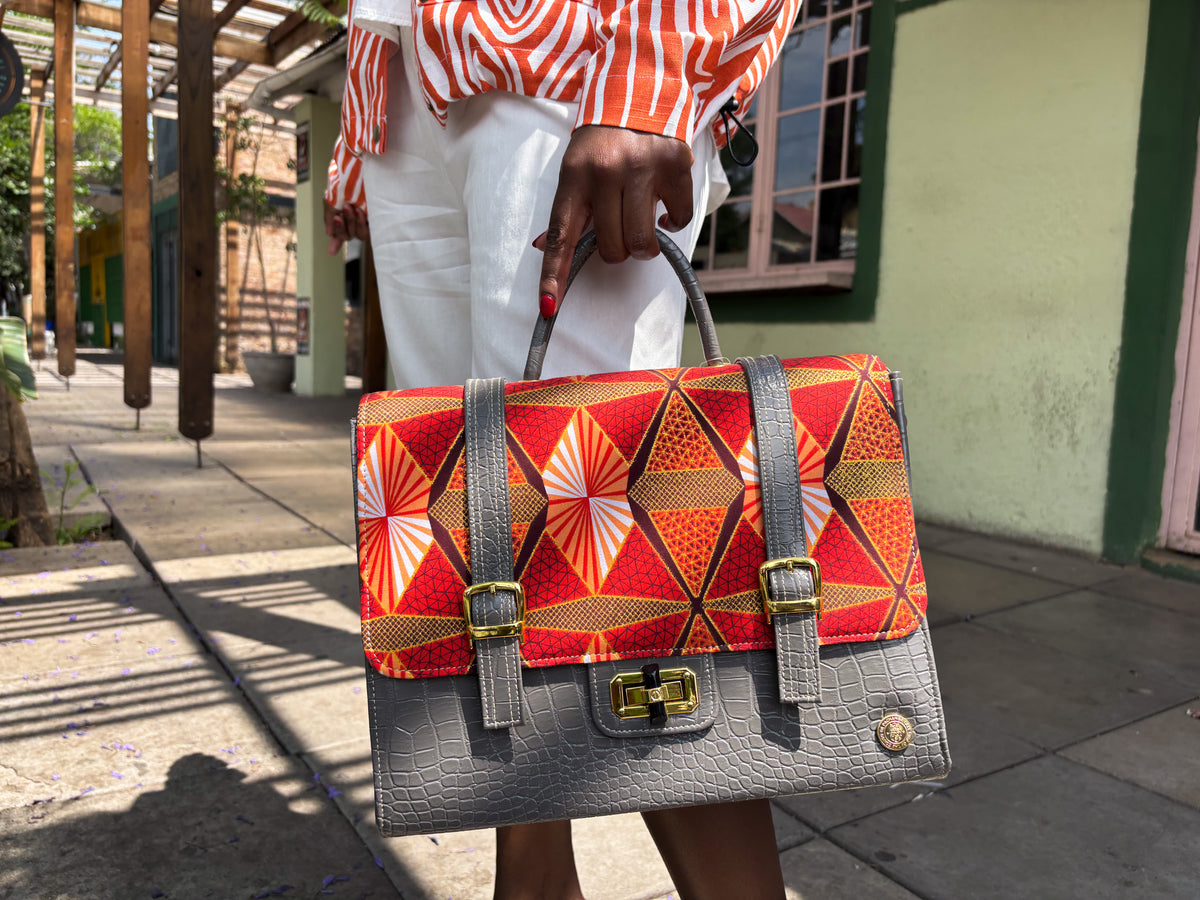 Grey vegan leather handbag or backpack with gold, red and orange African wax fabric inlay, two gold buckled clasps and a gold twist-lock.