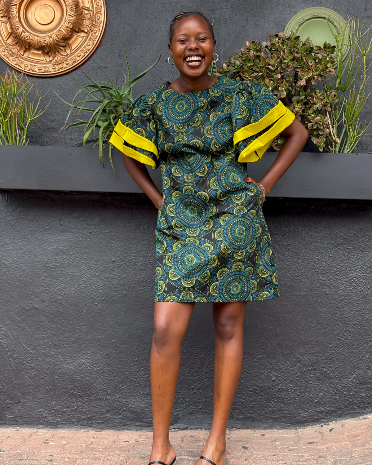 Smiling African woman wearing a Sam Dress in green.