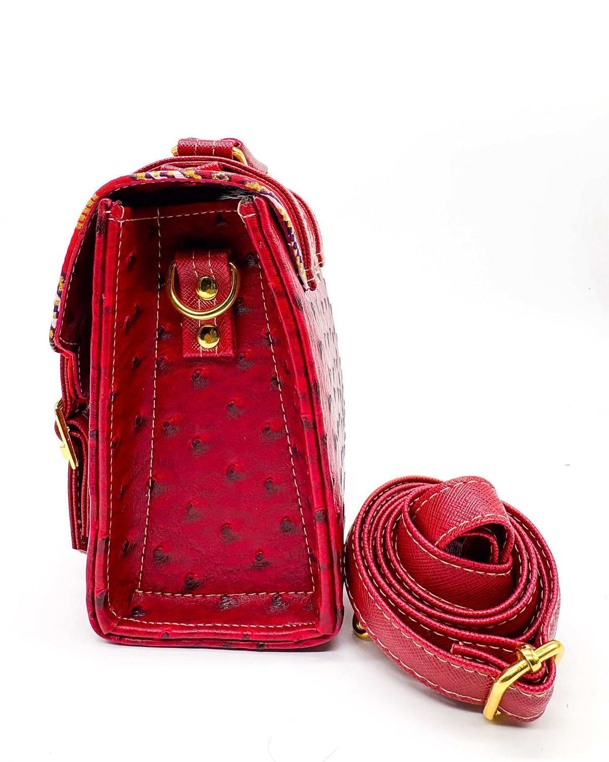 Side view, maroon vegan leather handbag or crossbody bag with red and gold African Wax fabric inlay, two gold buckles and magnetic clasp.
