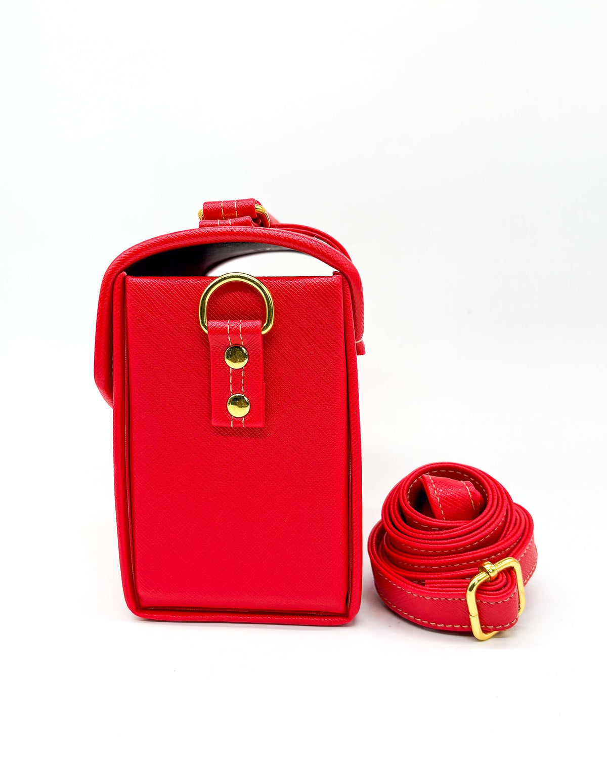 Side view, red vegan leather handbag or crossbody bag, with red, gold and white African Wax fabric inlay, a gold buckle and magnetic clasp.